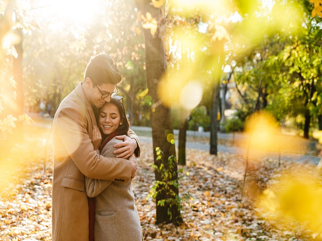 изображение молодой счастливой пары, улыбающейся и обнимающейся в осеннем парке